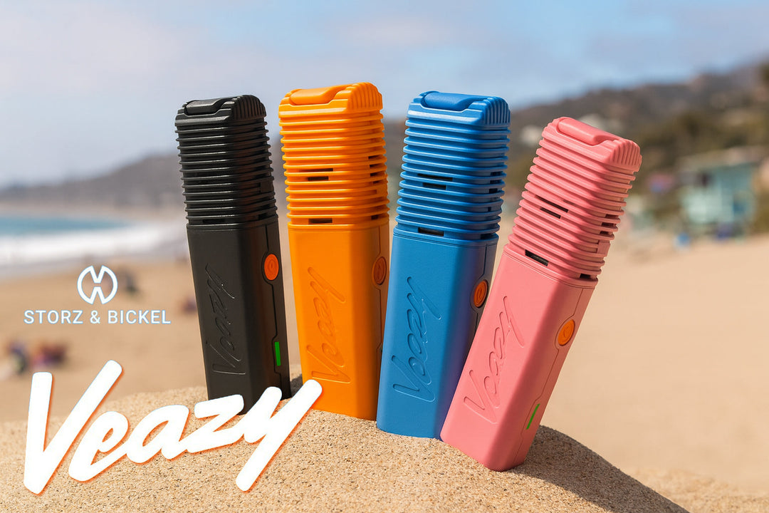 Storz & Bickel Veazy dry herb vaporizer lineup in all four colors — Alluring Black, Dynamic Blue, Inspiring Orange, and Charming Pink — displayed on a sunny Southern California beach, highlighting its compact, portable design and premium build.