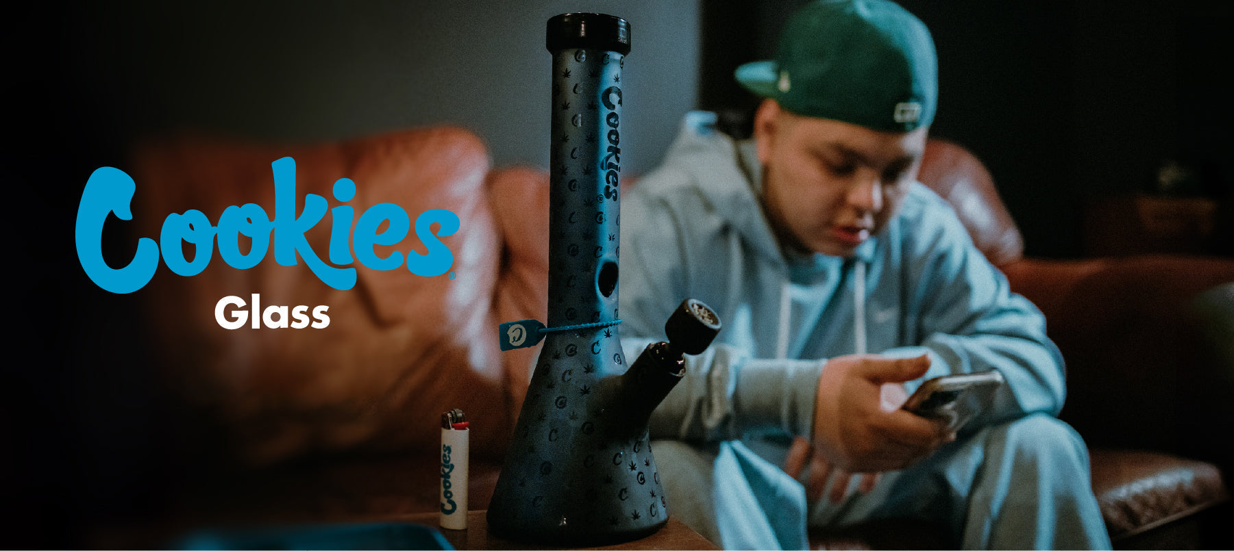 Cookies Glass Collection hero image featuring matte black Cookies water pipe on table beside lighter, cozy lounge scene background.