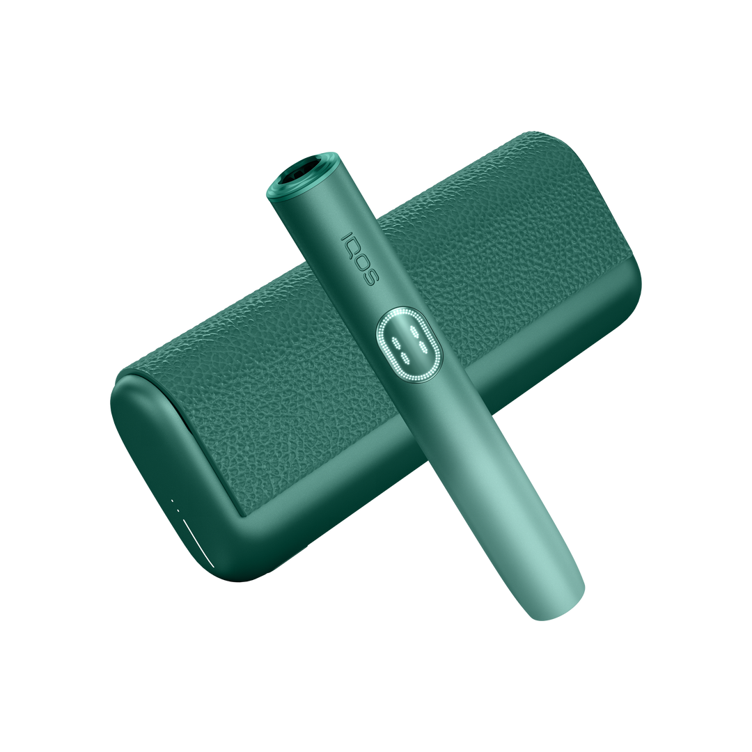 IQOS ILUMA i PRIME Aspen Green holder laid diagonally across the closed textured pocket charger