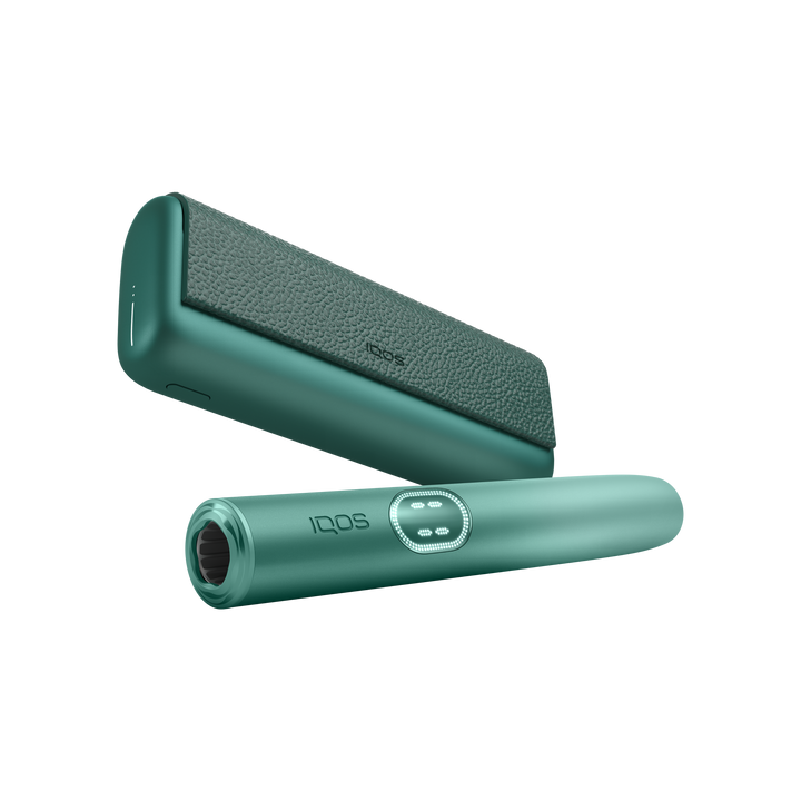 IQOS ILUMA i PRIME Aspen Green holder in front of the pocket charger, low angle showing the mouth end