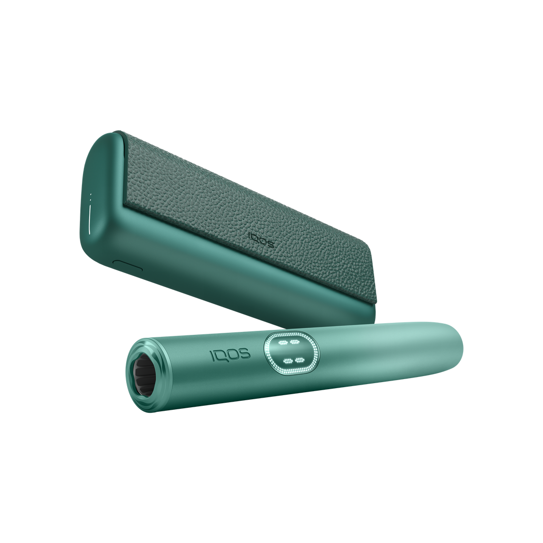 IQOS ILUMA i PRIME Aspen Green holder in front of the pocket charger, low angle showing the mouth end