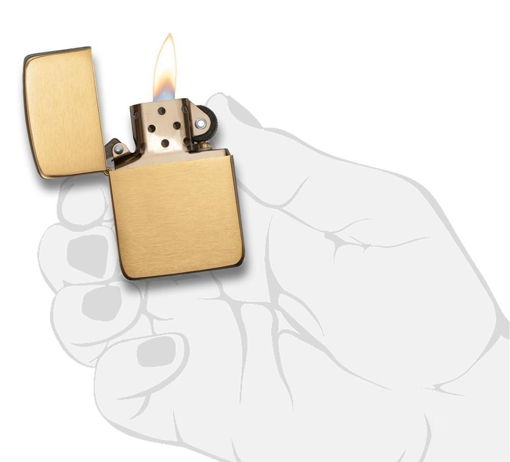 Zippo - 1941 Replica Brushed Brass Lighter with windproof flame, shown open and lit against a hand illustration background. Durable refillable gas lighter.
