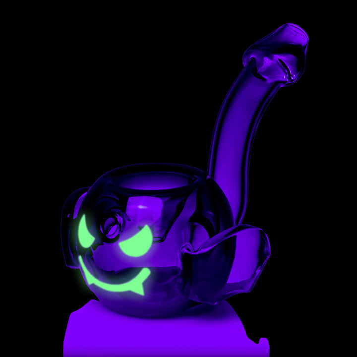 MJ Arsenal Bud-Sucker Hand Pipe under black light, the green face glowing, three-quarter view