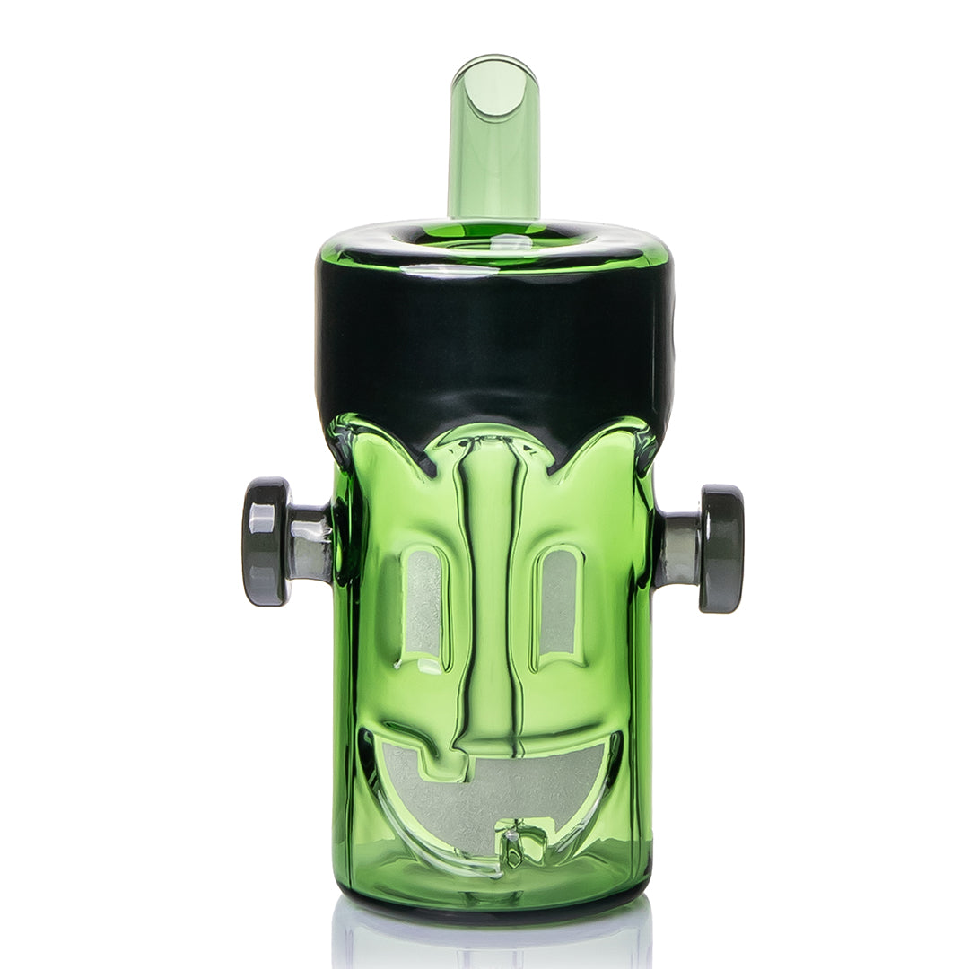MJ Arsenal Frankenbubbler front view, showing the monster face worked into the green glass in glow-in-the-dark material: two rectangular eyes and a wide grin with a single tooth, framed by the black flat top and the side bolts