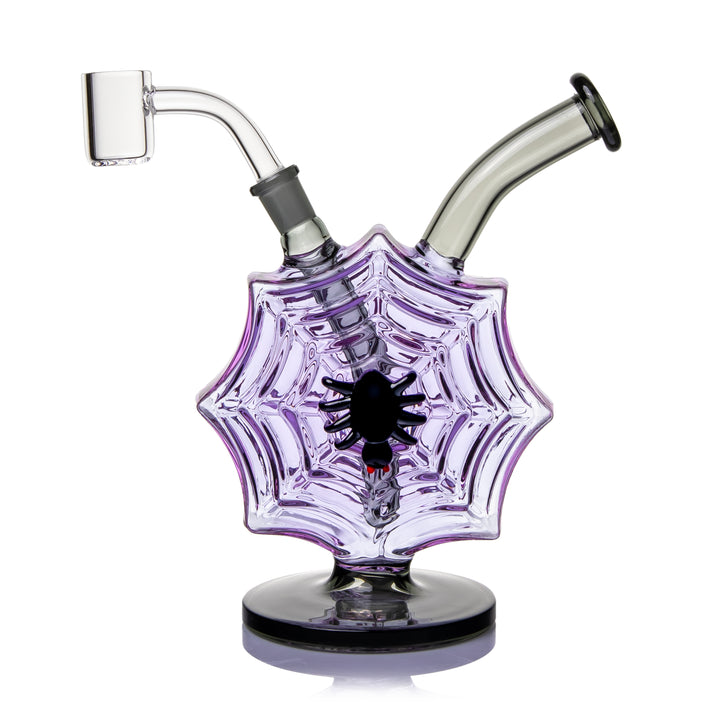MJ Arsenal Nightcrawler Mini Dab Rig, a 7.5 inch translucent purple spiderweb glass rig with a sculpted black spider on the face, smoke-colored mouthpiece, clear quartz banger fitted to the 10mm joint, and a round black base