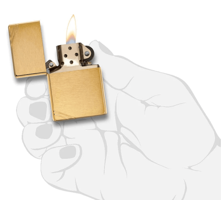 Zippo Brass Vintage lighter with brushed brass finish and slashes, shown lit in a hand illustration. Windproof and refillable design.